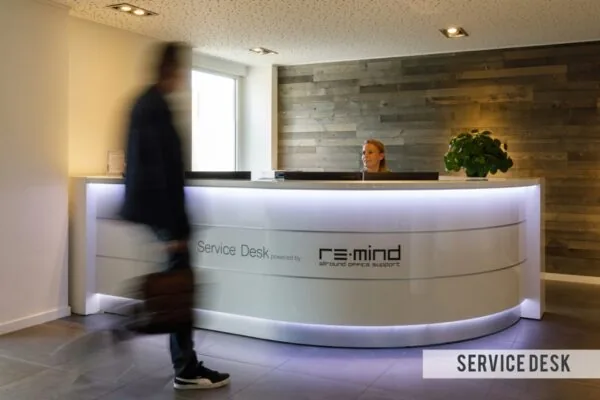 Een man loopt langs de receptiebalie van de service desk van Re:mind in een modern kantoorpand aan de Baarnsche Dijk.